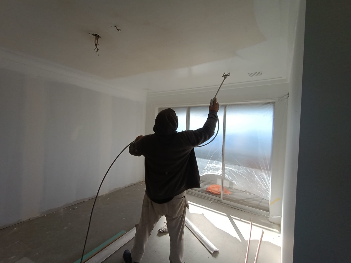 Painter spray-applying wall and ceiling finish at fit-out stage